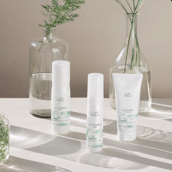 Collection of Wella NutriCurls products are on a white surface with glasses vases behind them.