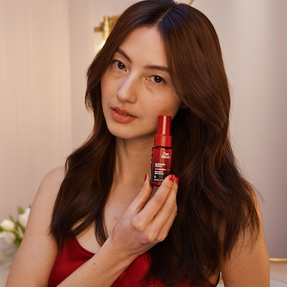 Model with long, straight, dark brown hair holds up a bottle of ULTIMATE REPAIR Night Serum.