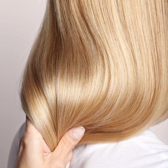 Close-up of a hand clasped around the mid-lengths of a person's light blonde hair