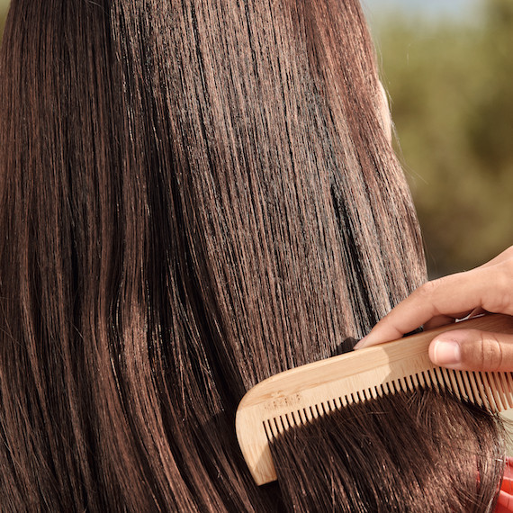 Close-up of a wooden comb being brushed through the mid-lengths of light brown, straight hair