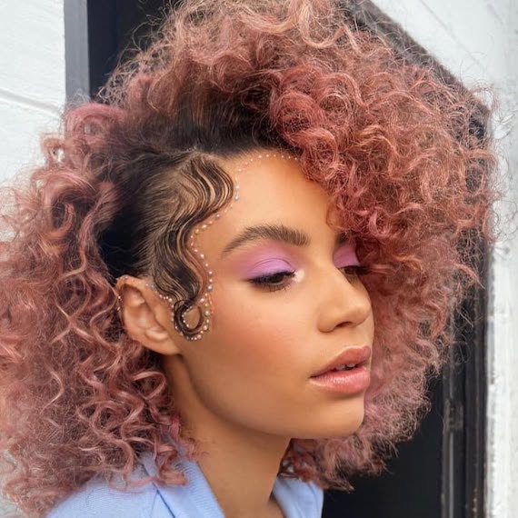 Model with dark, curly hair featuring dusty pink tones through the lengths.