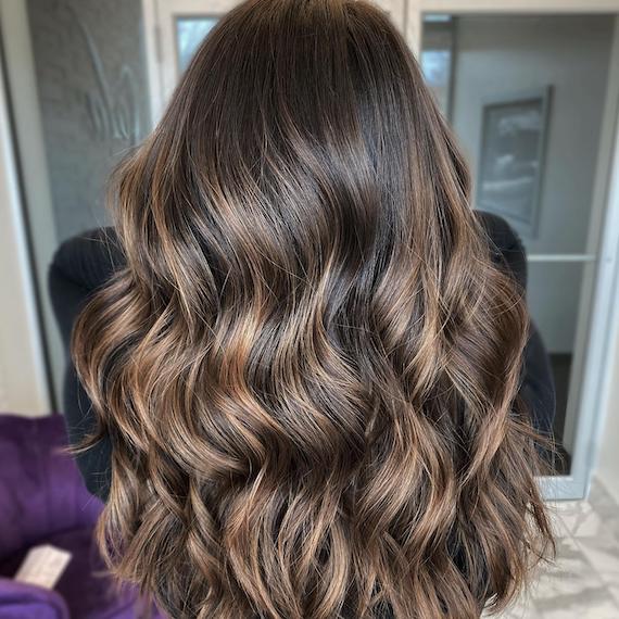 Back of woman’s head with espresso brown, wavy hair and light hazelnut highlights.