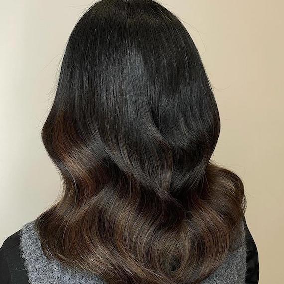Back of woman’s head with wavy espresso hair colour and subtle balayage.