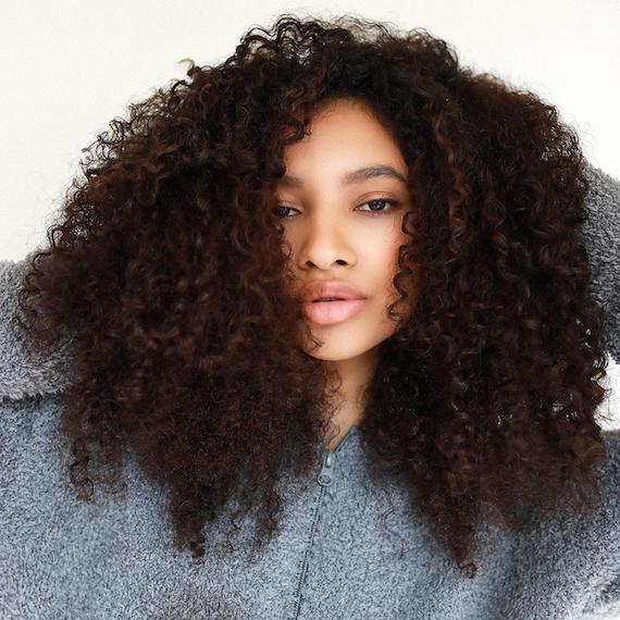 Woman faces the camera with espresso brown, curl hair and subtle highlights.