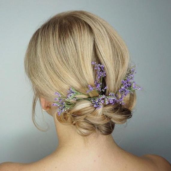 Back of woman’s head with blonde hair in a low bun, accessorised with flowers.