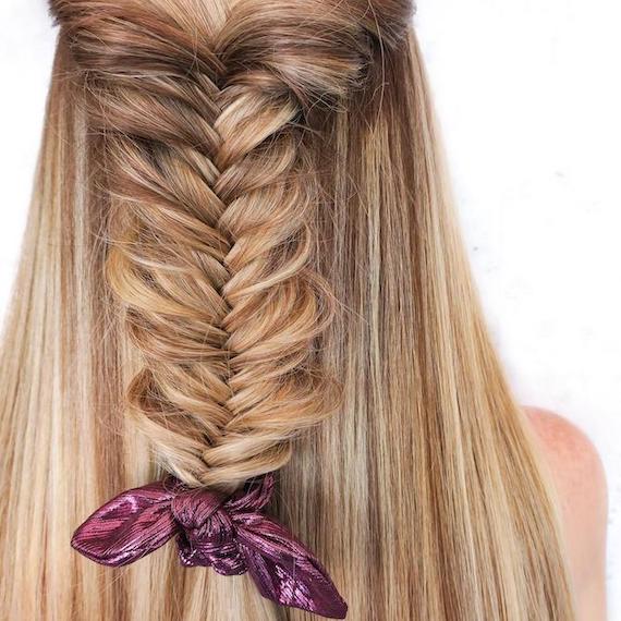 Back of woman’s head with fishtail braid through hair, tied with a metallic scrunchie.