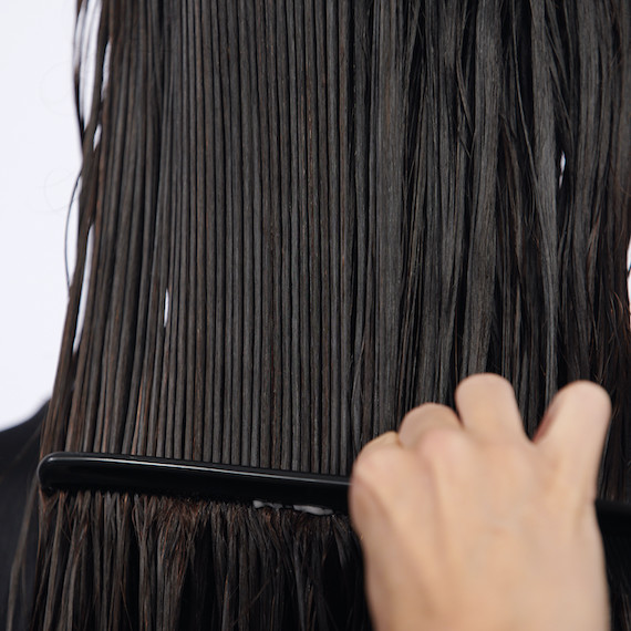 Close-up of a comb running through dark brown, wet hair.