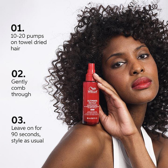 Model with black, curly hair holds up a bottle of ULTIMATE REPAIR Miracle Hair Rescue.