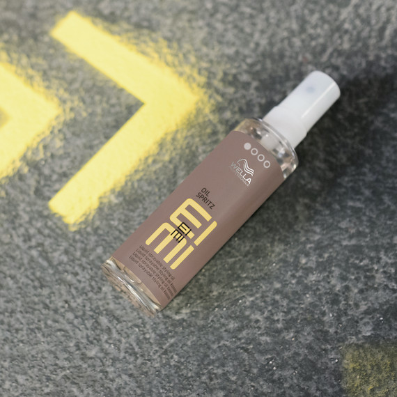EIMI Oil Spritz bottle lies flat on a concrete surface. 