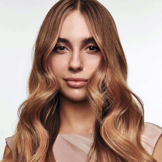 Model with long, loosely curled, brown-blonde hair featuring rose gold balayage.