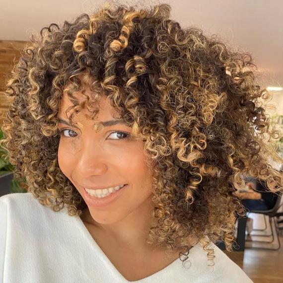 Woman with curly hair and golden blonde highlights smiles at the camera.