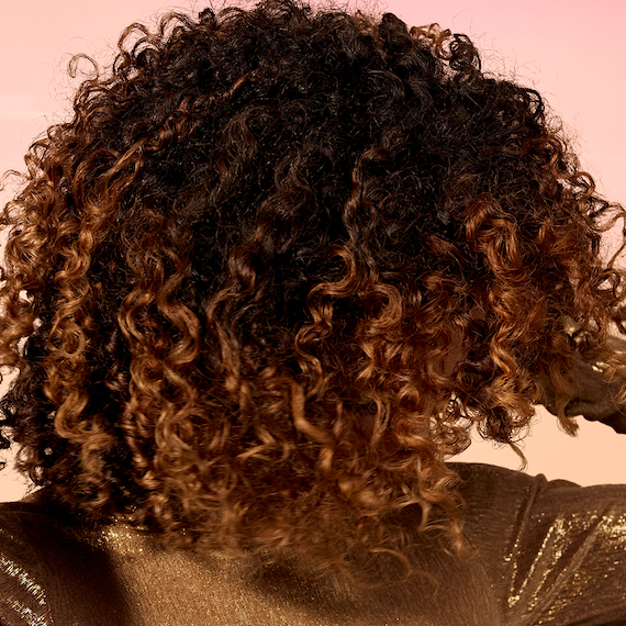 Close-up of model’s brown curly hair featuring bronze highlights.