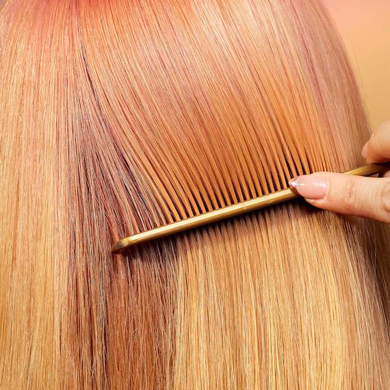 Close-up of a comb running through rose gold hair.