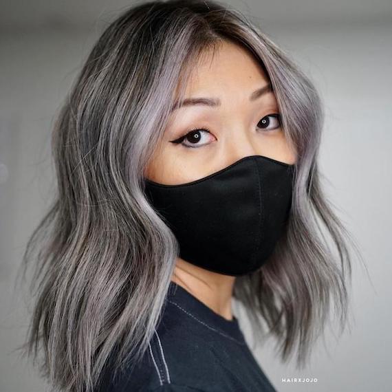 Woman wearing a black face mask. Her hair gray brown hair, created using Wella Profes-sionals, is styled in loose waves.