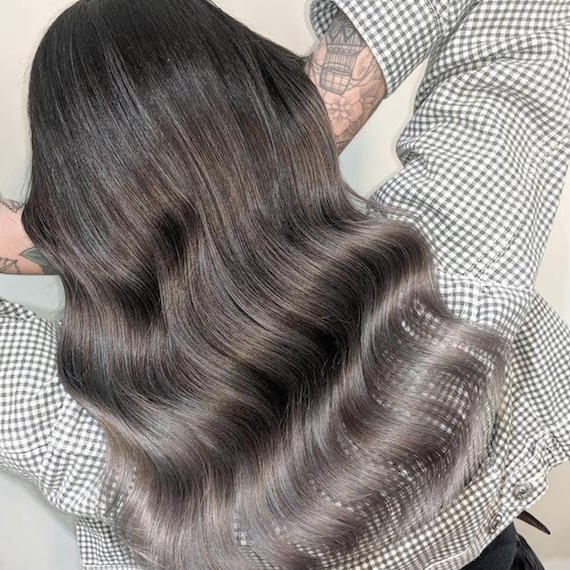 Back of woman’s head with long, wavy, black to gray ombre hair, created using Wella Professionals.