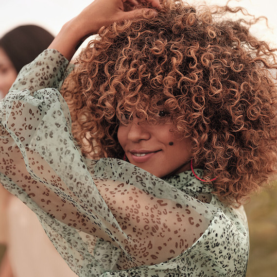 Woman runs hand through curly, caramel brown hair.