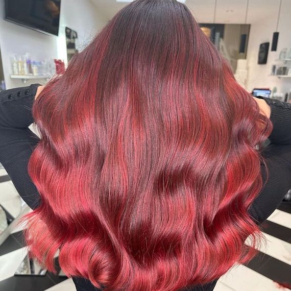 Back of model’s head with long, wavy, dark hair featuring cherry cola highlights.