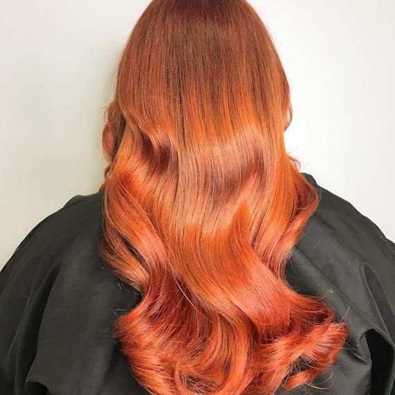 Photo of the back of a woman’s head with copper, wavy hair, glossed using Wella Professionals