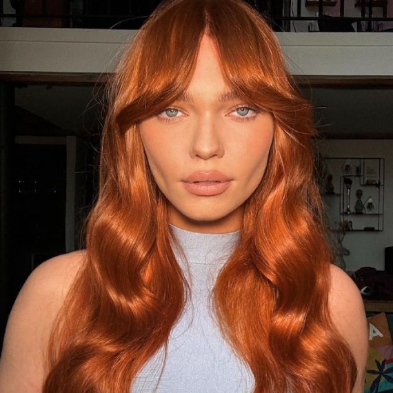 Model with ultra-shiny, copper red, loosely saved hair.