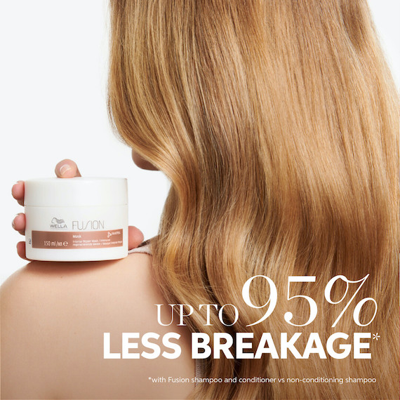 Model with long, glossy, blonde hair holds up Fusion Mask, which gives you up to 95% less breakage.