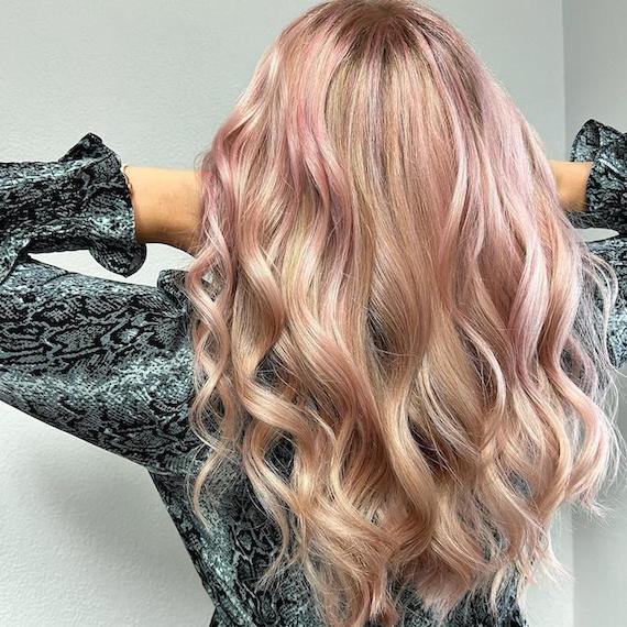 Back of woman’s head with long, loosely curled, pink blonde hair.