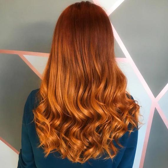 Back of a woman’s head showing long, wavy, pumpkin spice hair, created using Wella Professionals. 