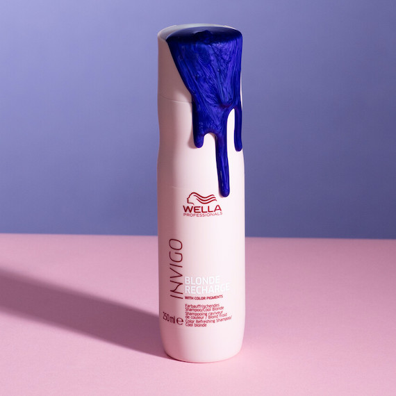 A bottle of INVIGO Blonde Recharge Cool Blonde Shampoo with purple shampoo pouring out.