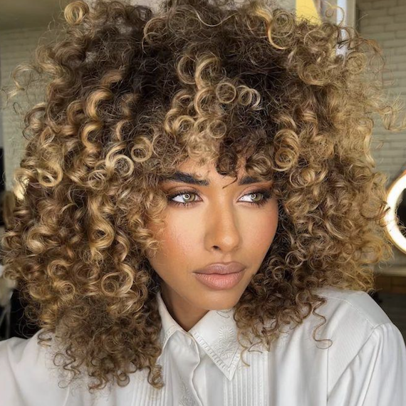 Headshot of a person with very curly brown-blonde hair that's been colored using the high contrast balayage technique