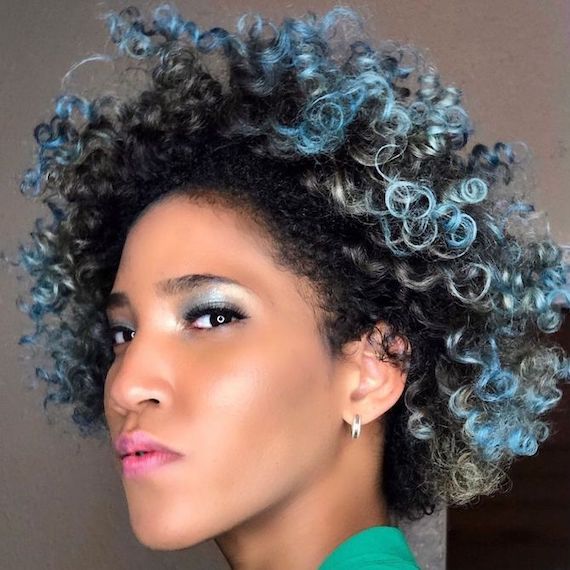 Model with short, curly, black hair and electric blue highlights looks directly into the camera.