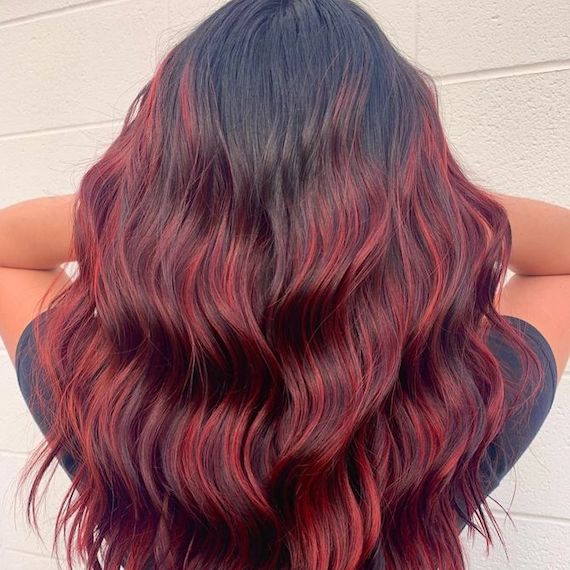 Back of model’s head with long, tousled, black hair and cherry red balayage highlights.