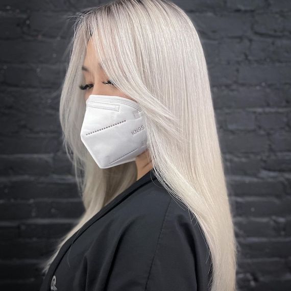 Model with long white blonde hair faces the side wearing a face mask.