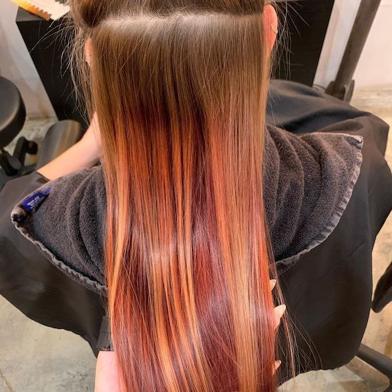 Person sits in a salon chair to get their red highlights transformed to all over ice blonde.