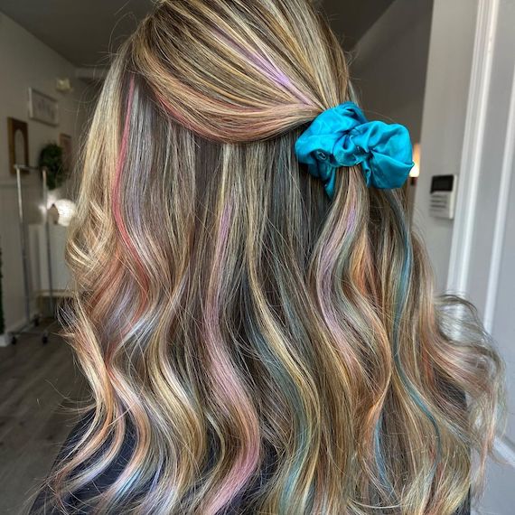 Back of person's head. They have dirty blonde hair with holographic pastel highlights tied with a blue scrunchie