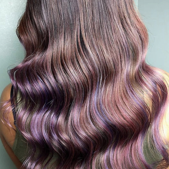 Close-up of long, wavy dark hair with holographic colors painted in using the balayage technique
