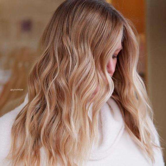 Headshot of a person with blonde hair and a warm honey balayage. Their face is largely concealed by their hair