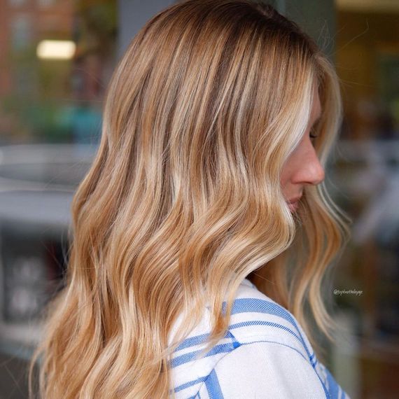 Profile of a person with long blonde hair colored with honey highlights and a dark root shadow. 