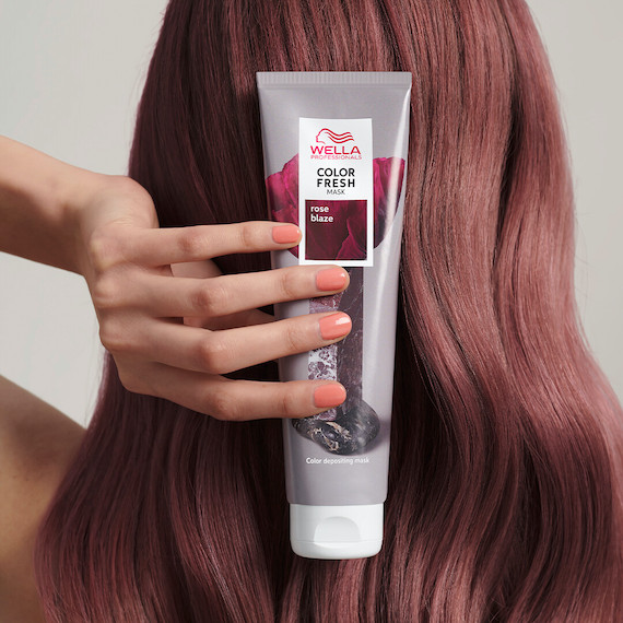 Model with rose brown hair holds up a tube of the Color Fresh Mask in Rose Blaze.