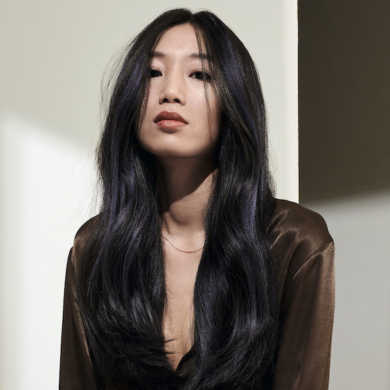 Model with long, wavy, black hair and violet highlights faces the camera.