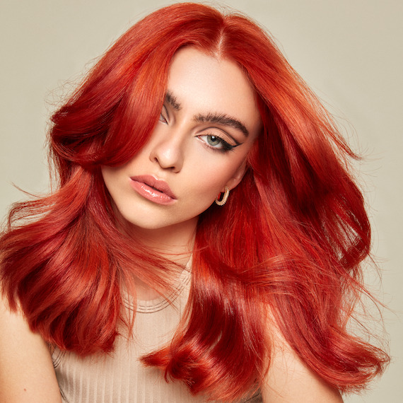 Model with mid-length, fiery red hair and winged eyeshadow faces the camera.