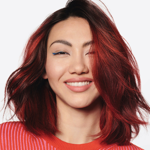 Model with short, cherry red, wavy hair smiles at the camera.