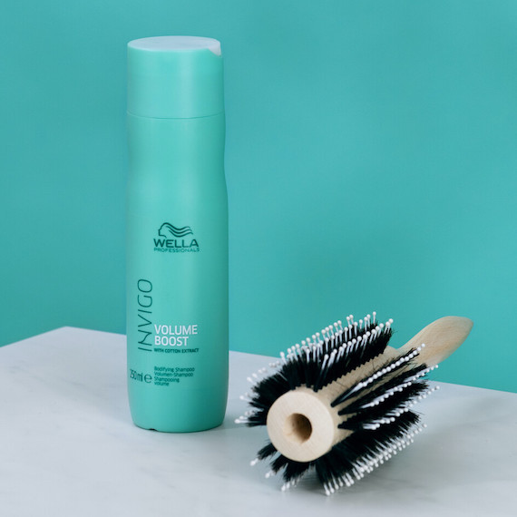 A bottle of INVIGO Volume Boost Bodifying Shampoo next to a hairbrush.