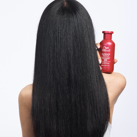 Hinterkopf eines Modells mit langem, glattem, glänzendem schwarzem Haar. Sie hält eine Flasche Ultimate Repair Shampoo in der Hand.