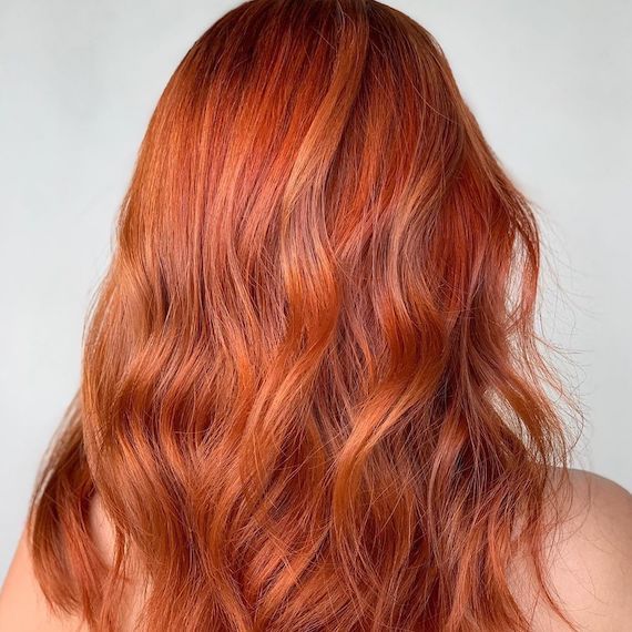 Back of model’s head with long, glossy, wavy, copper hair.