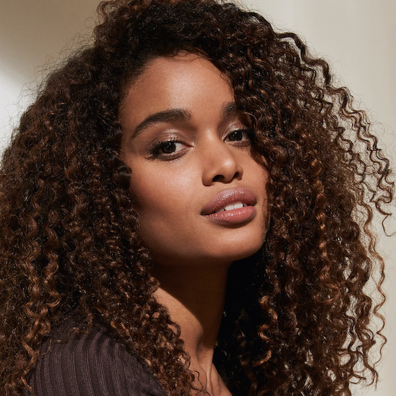 Model with thick, curly, brown hair faces the camera.
