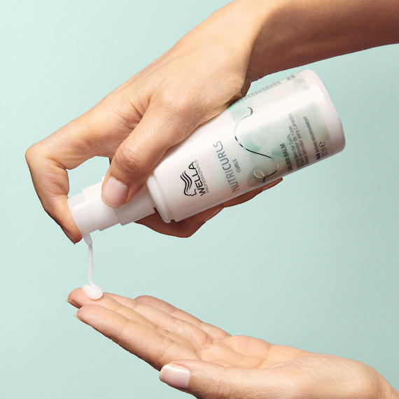NutriCurls Curlixir Balm is poured into palm of model’s hand.