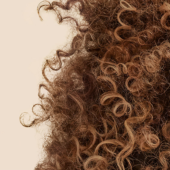 Model uses fingertips to smooth and detangle curly, brown hair.