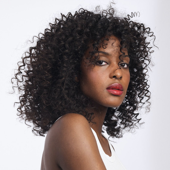 A model with shoulder-length, black, curly hair looks directly into the camera.