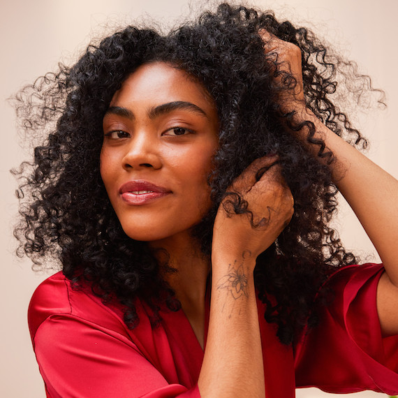 A model applies ULTIMATE REPAIR Night Serum to their dark, curly hair.