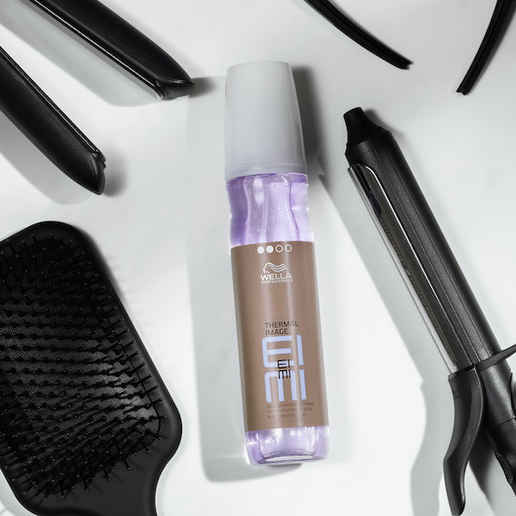 Bottle of EIMI Thermal Image heat protection spray surrounded by hair styling tools. 