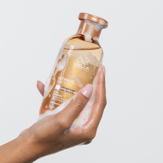 Model holds a bottle of ULTIMATE SMOOTH Shampoo.